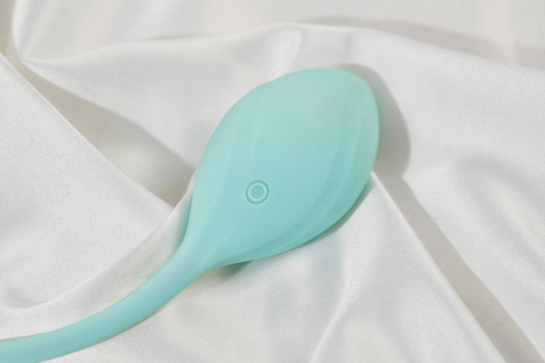 A sleek teal lemon clitoral vibrator resting on white silk, symbolizing intimate pleasure and partnership