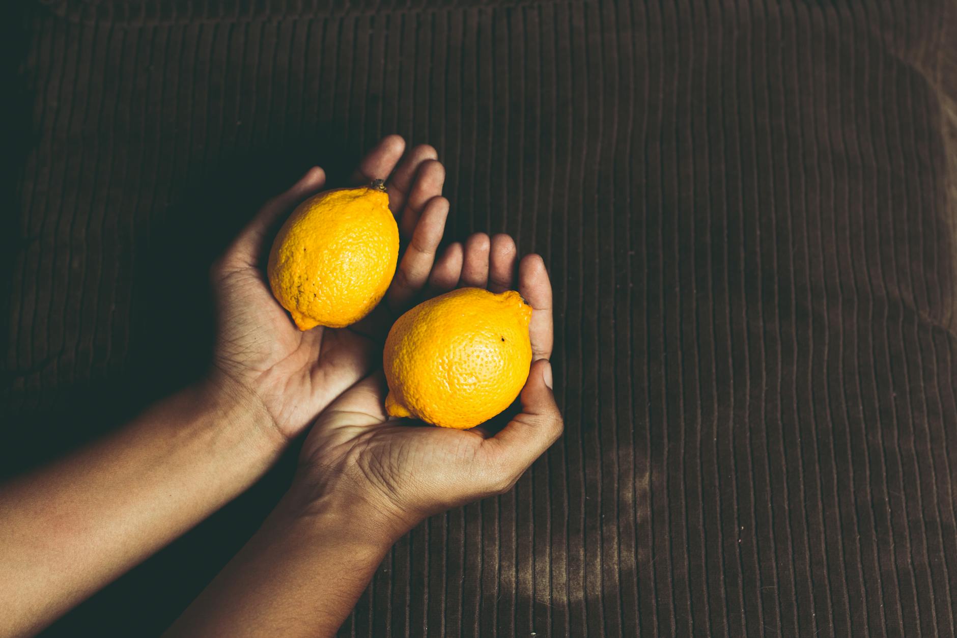 Hand holding a fresh lemon against a yellow background, symbolizing freshness and citrus vibrancy.