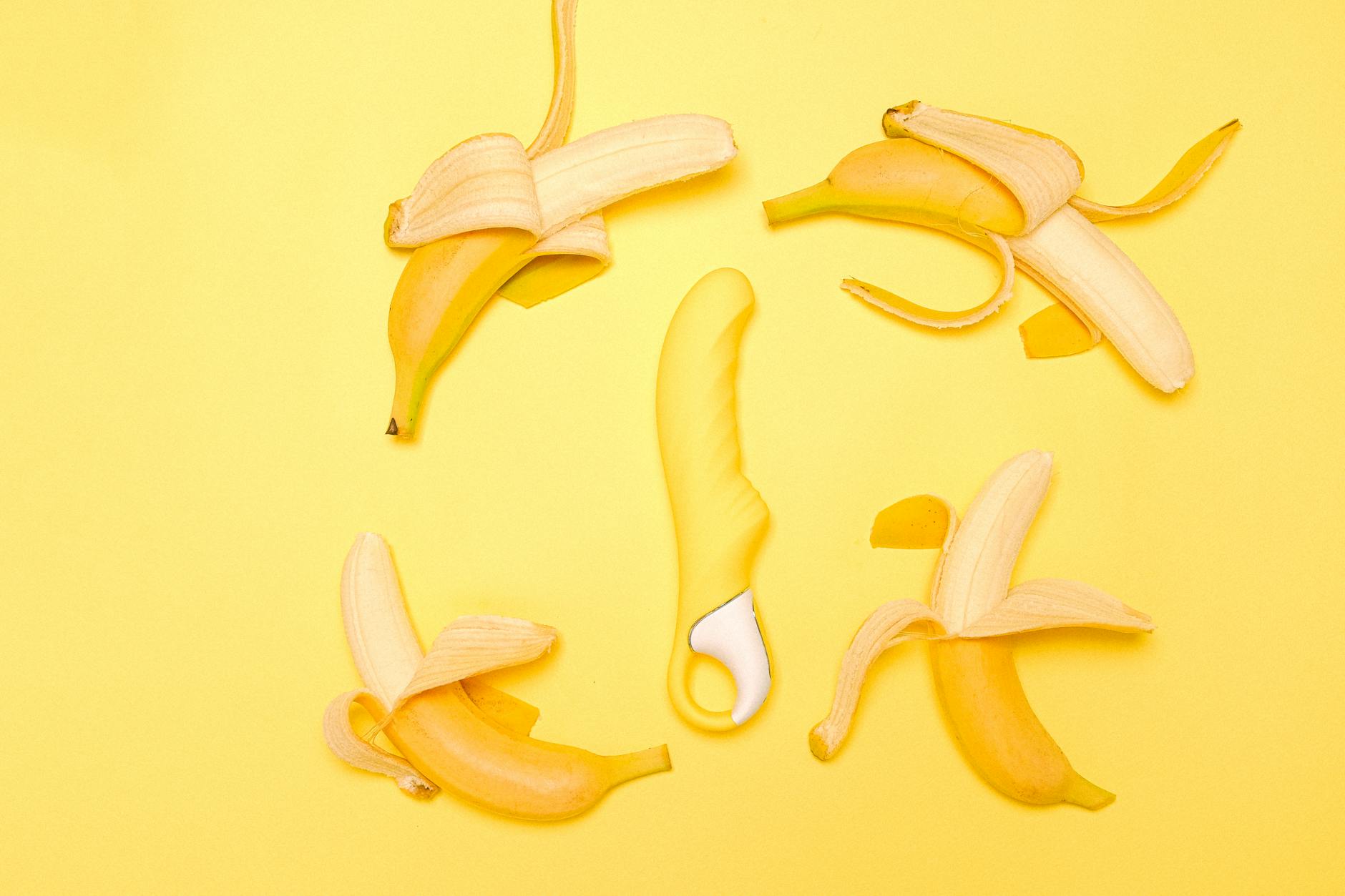 Yellow silicone lemon vibrator surrounded by peeled lemons on yellow background