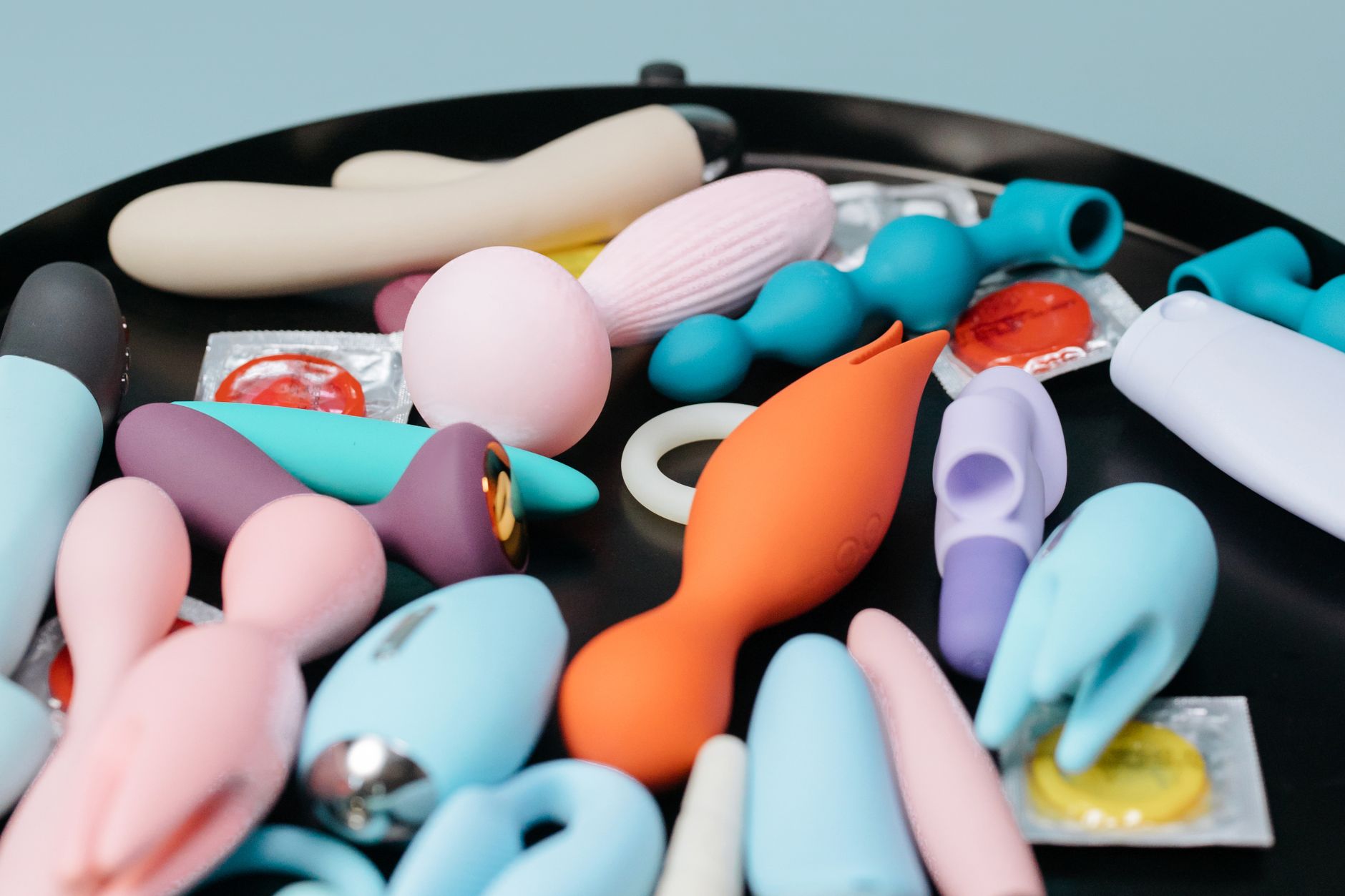 Two hands holding pink and blue clitoral vibrators against a pastel background