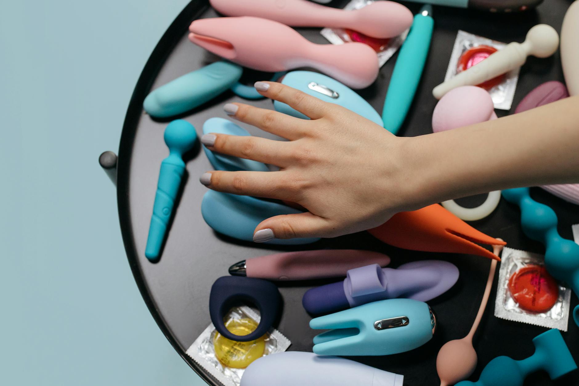 Manos sosteniendo varios juguetes sexuales de colores pastel