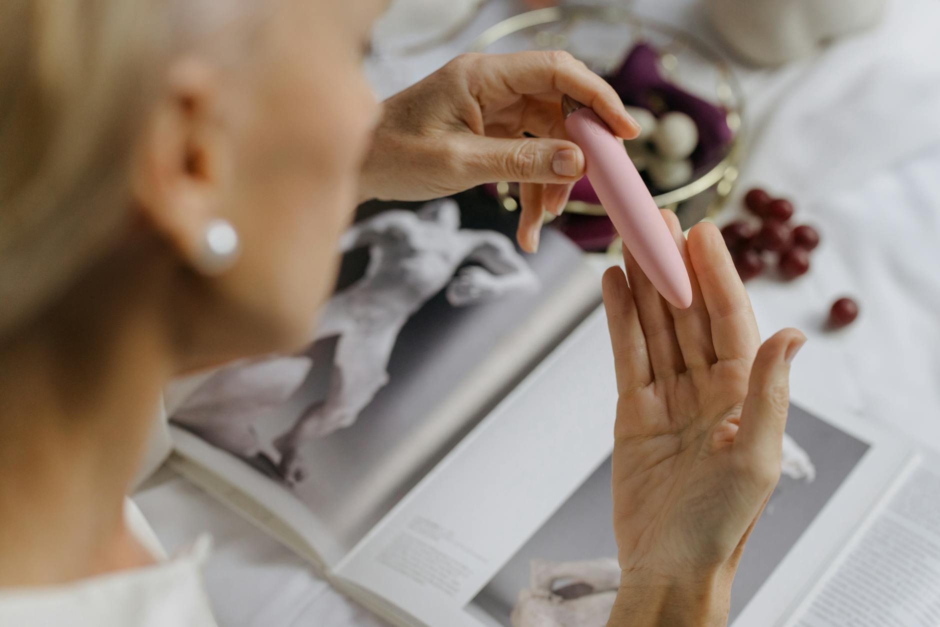 Close-up of a person holding a pink vibrator next to art books, symbolizing personal exploration and intimate communication