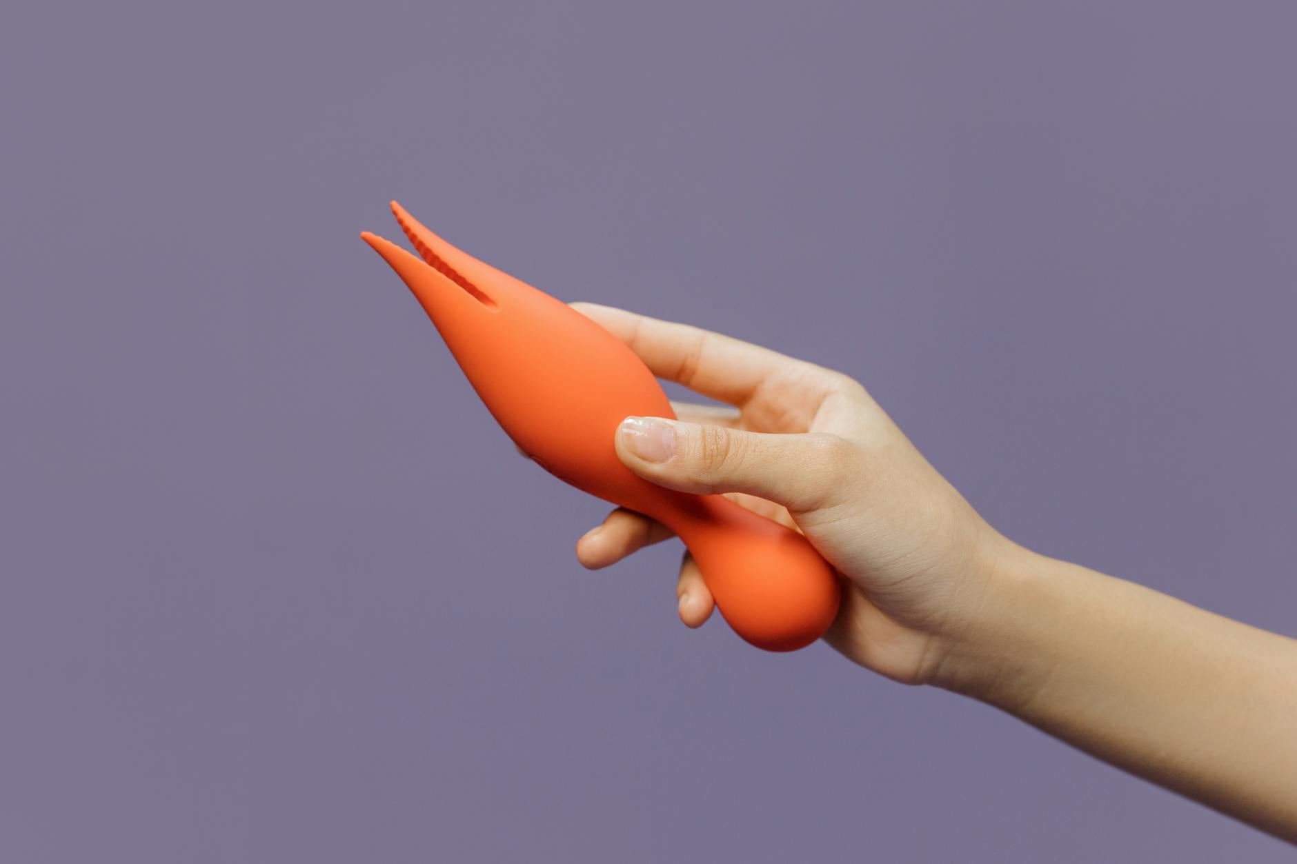 A hand holding a lemon clitoral vibrator against a minimalistic purple backdrop, showcasing modern sensuality and design