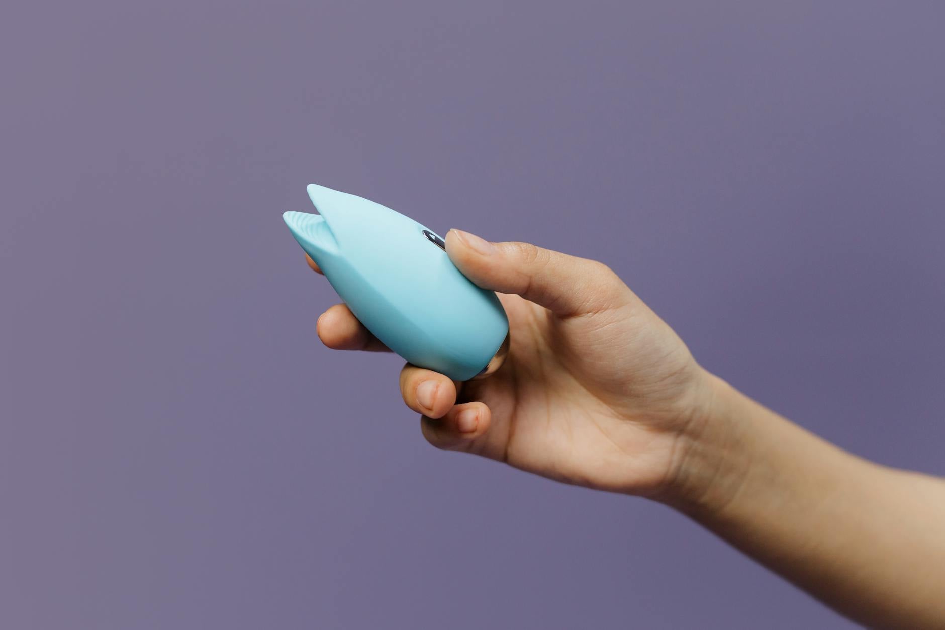 Intimate close-up of hands holding a sleek blue vibrator against a purple background
